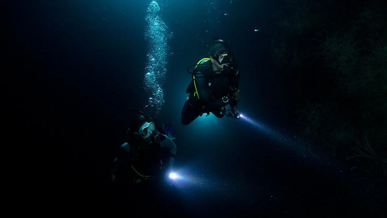 Divers during a night scuba dive in the blackness of the Pacific Ocean off of the coast of Potrero, Guanacaste, Costa Rica