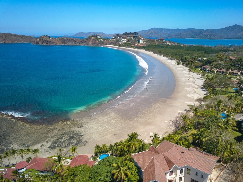 A glimpse of Playa Flamingo from drone view with the shore and the town of Flamingo on the right and the Pacific Ocean on the left